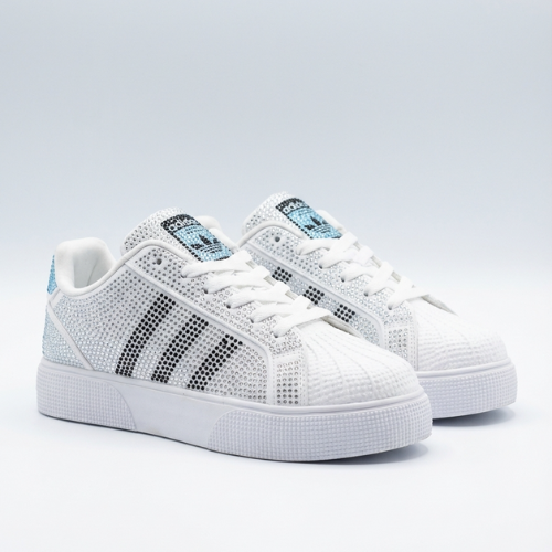 Paire de sneakers basses ornées de strass, posées sur un fond uni, vue trois-quarts avant. 