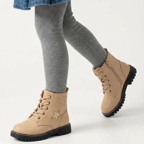 Fillette portant des bottes beige à semelle crantée, décorées d’une étoile glitter, look hiver confortable.