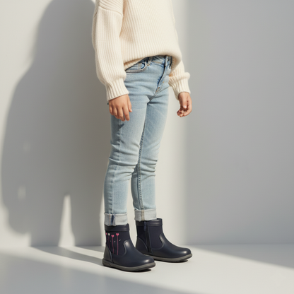 Petite fille portant des bottines bleu marine brodées, marchant dans un parc ensoleillé.